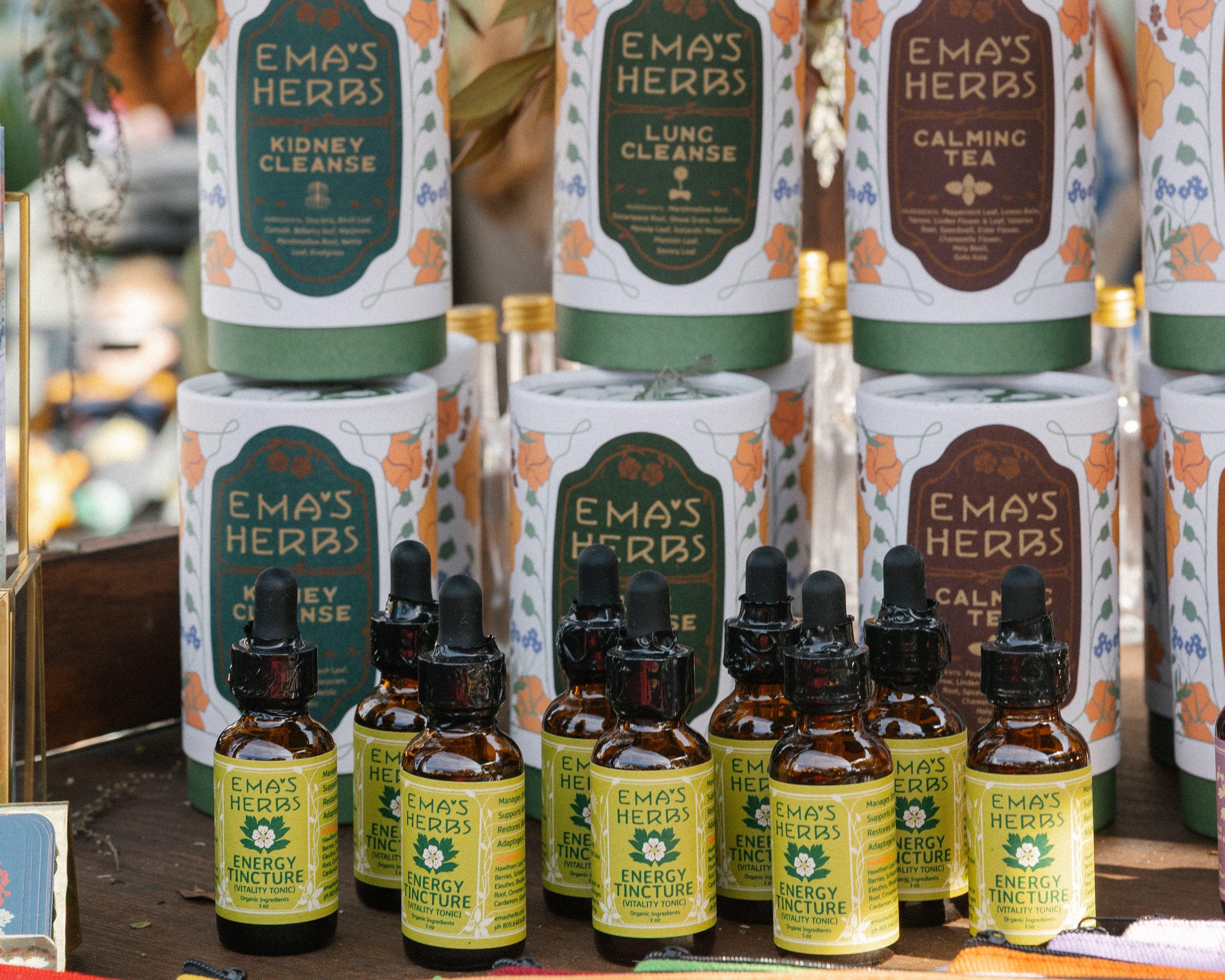 Ema's Herbs products including bottles and boxes displayed on a table with decorative elements.