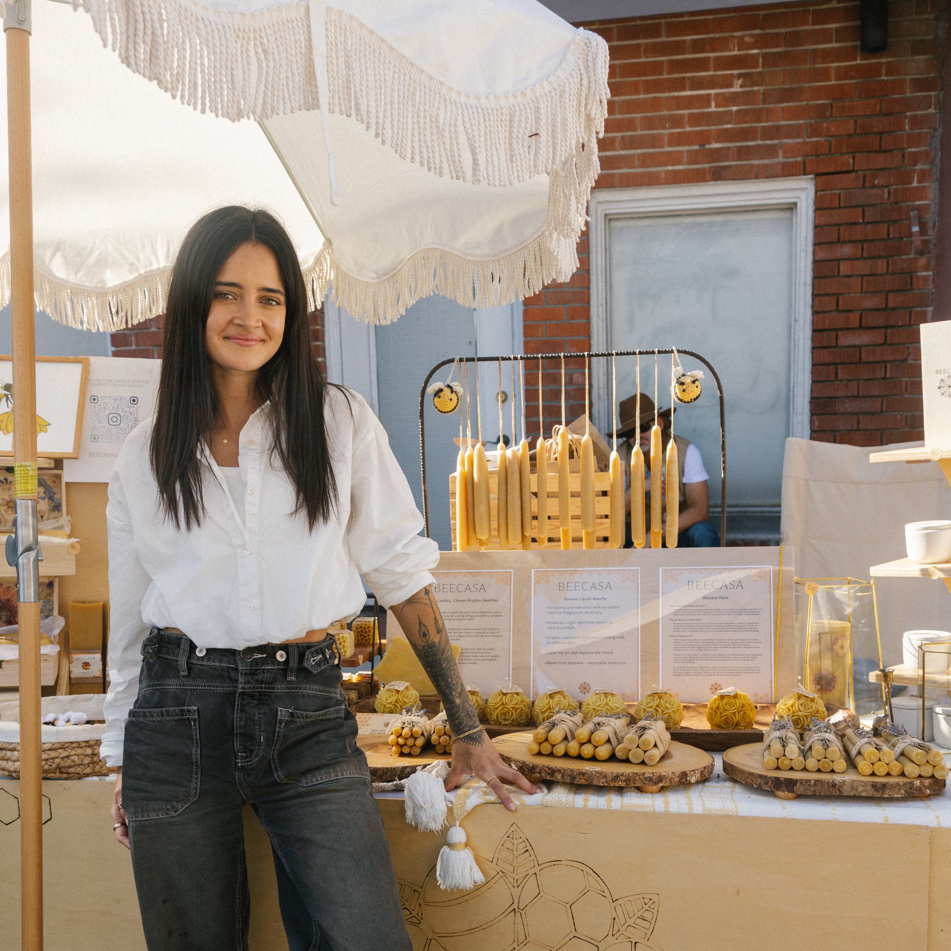 Woman standing next to a food display with a white umbrella and brick building in the background