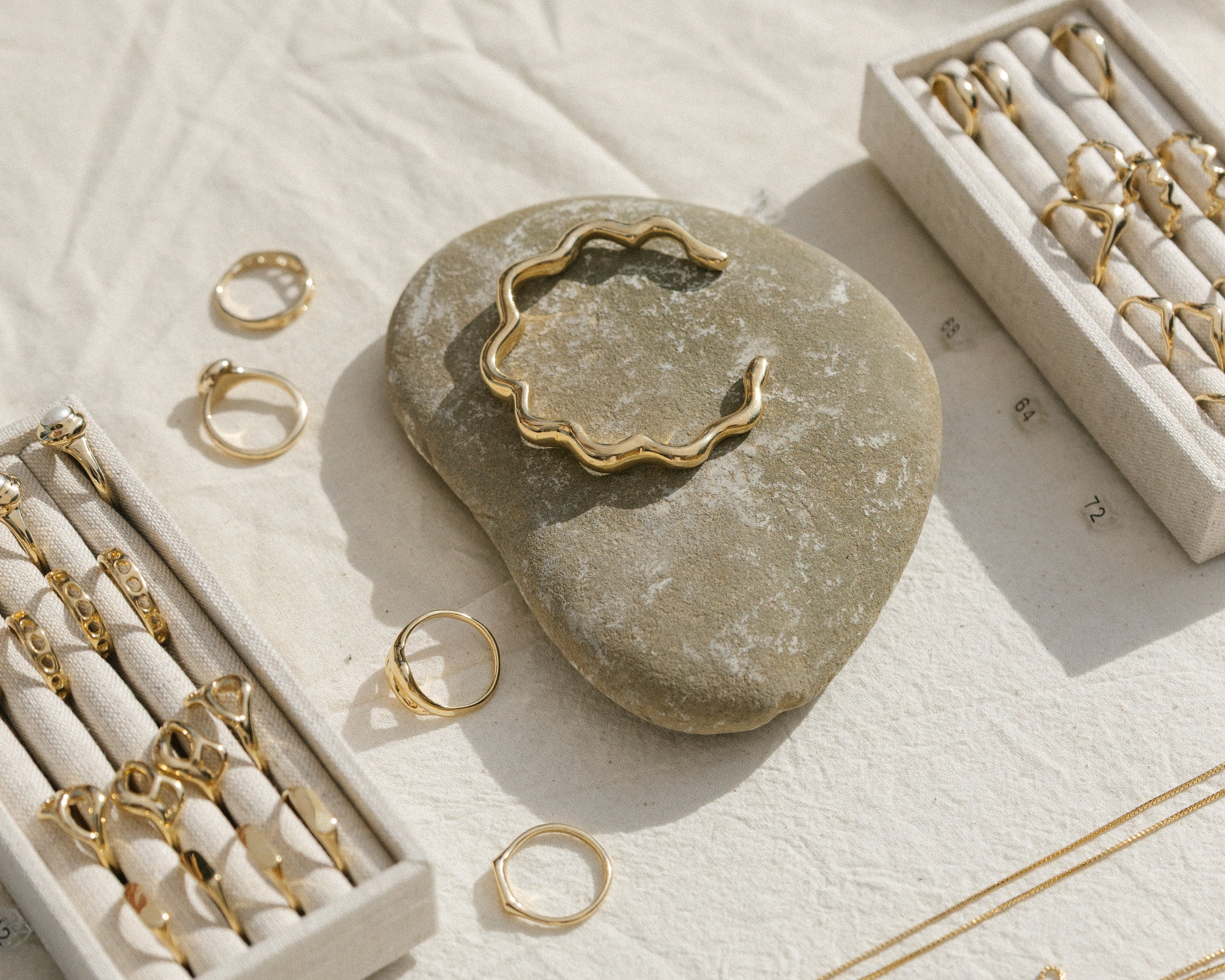 Gold jewelry including rings and necklaces on a textured surface with a stone and small box.