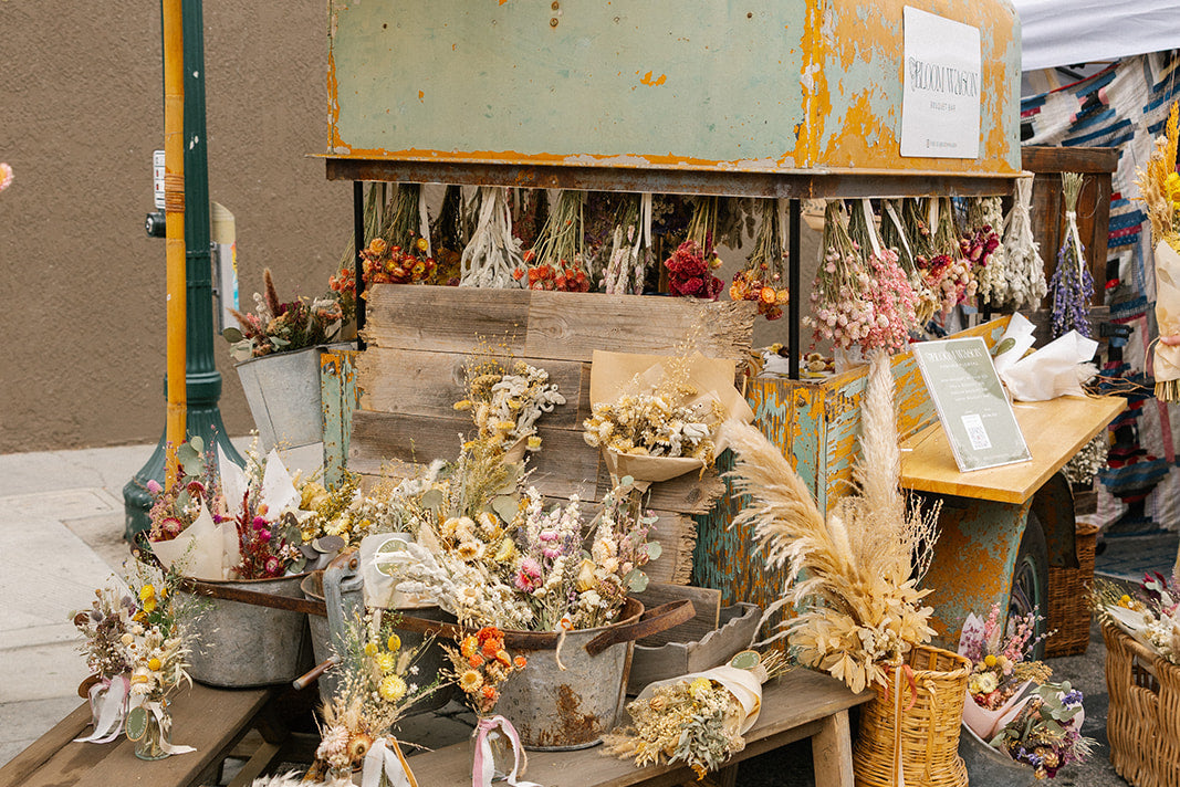 Vintage-style cart with floral arrangements and a yellow umbrella on a street setting.