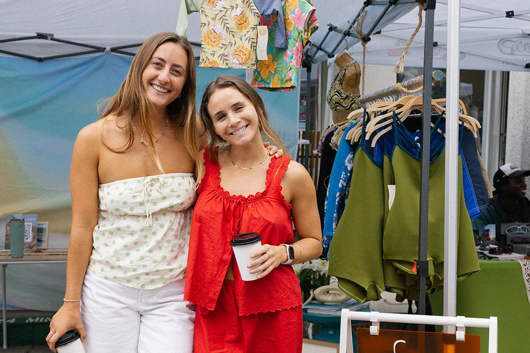 Two women standing next to a clothing booth at an outdoor event.