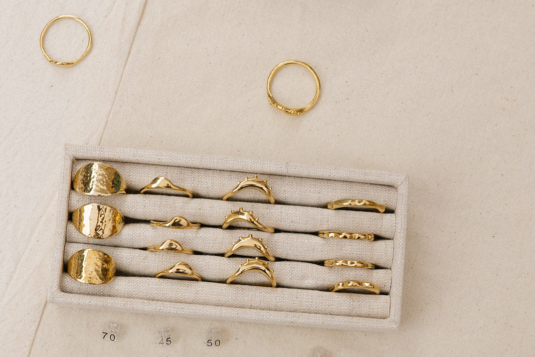 Set of gold rings in a display case on a beige surface with stone-like objects.